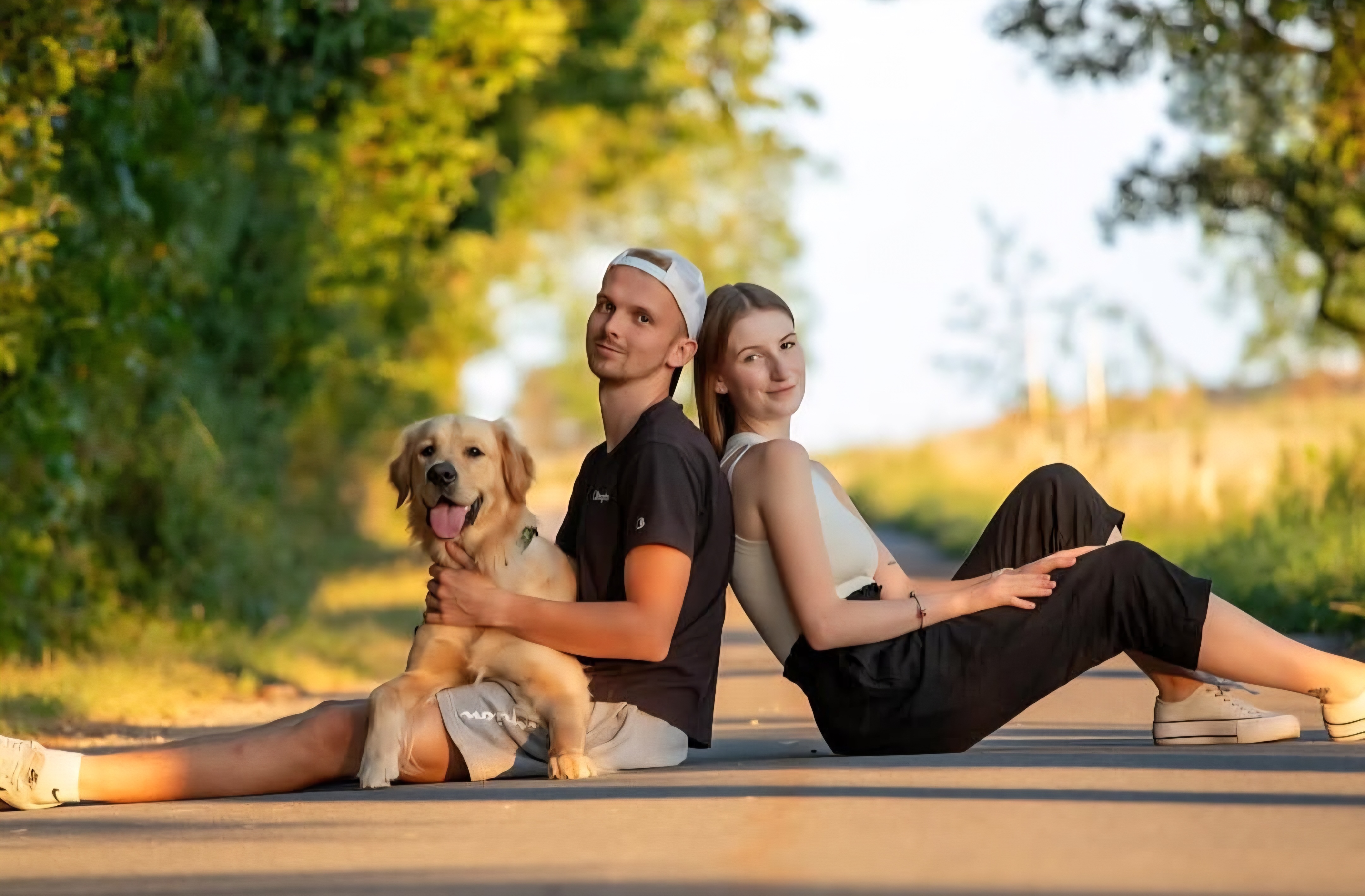 Pár se zlatým retrívrem při západu slunce na venkovské cestě